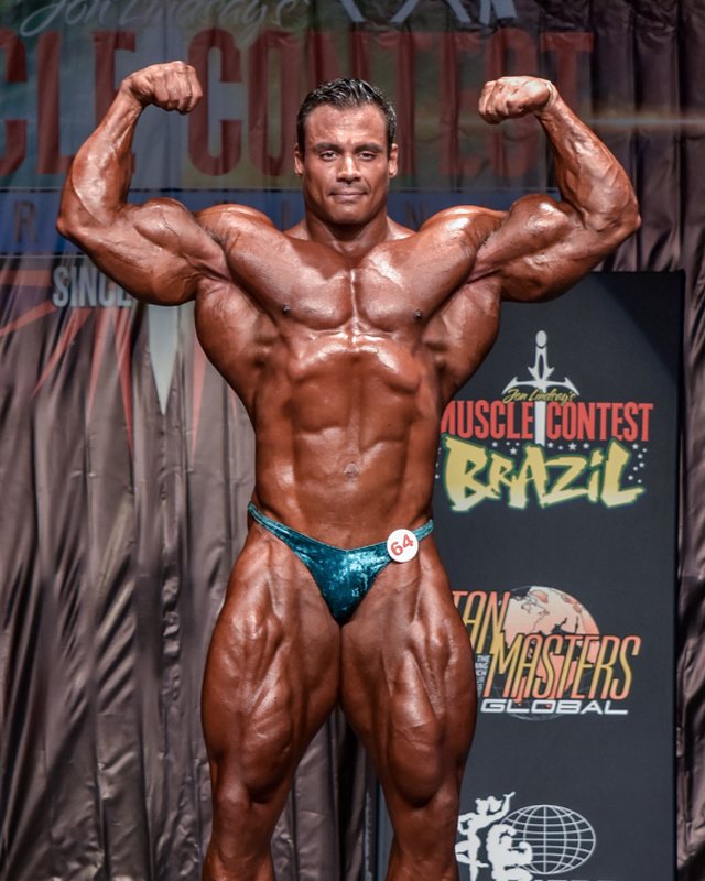 James Bondi em pose de duplo bíceps frontal no palco do Muscle Contest Brazil